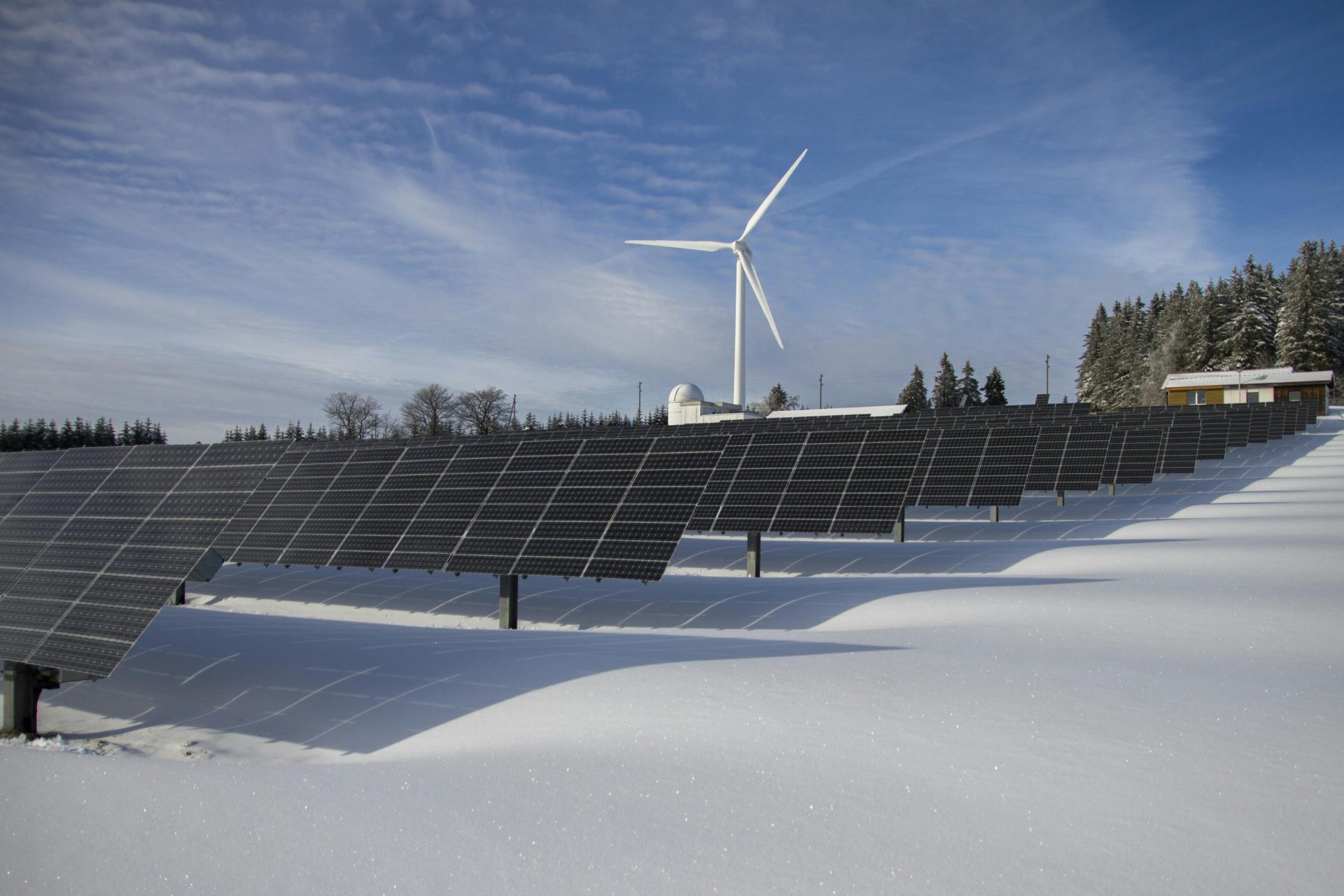 Solarpaneele und Windkraftanlage in einer verschneiten Landschaft, die erneuerbare Energiequellen demonstrieren.